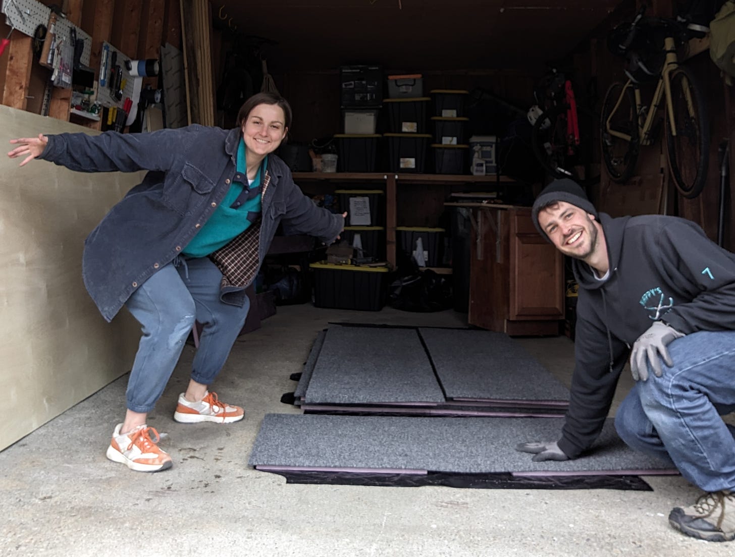 Author and her husband posing in their garage next to 4 sheets of XPS foam they recently upholstered to use in their truck camper