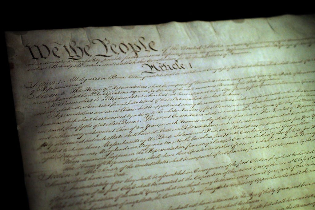 A handwritten copy of the U.S. Constitution with the iconic words "We the People" prominently visible. 