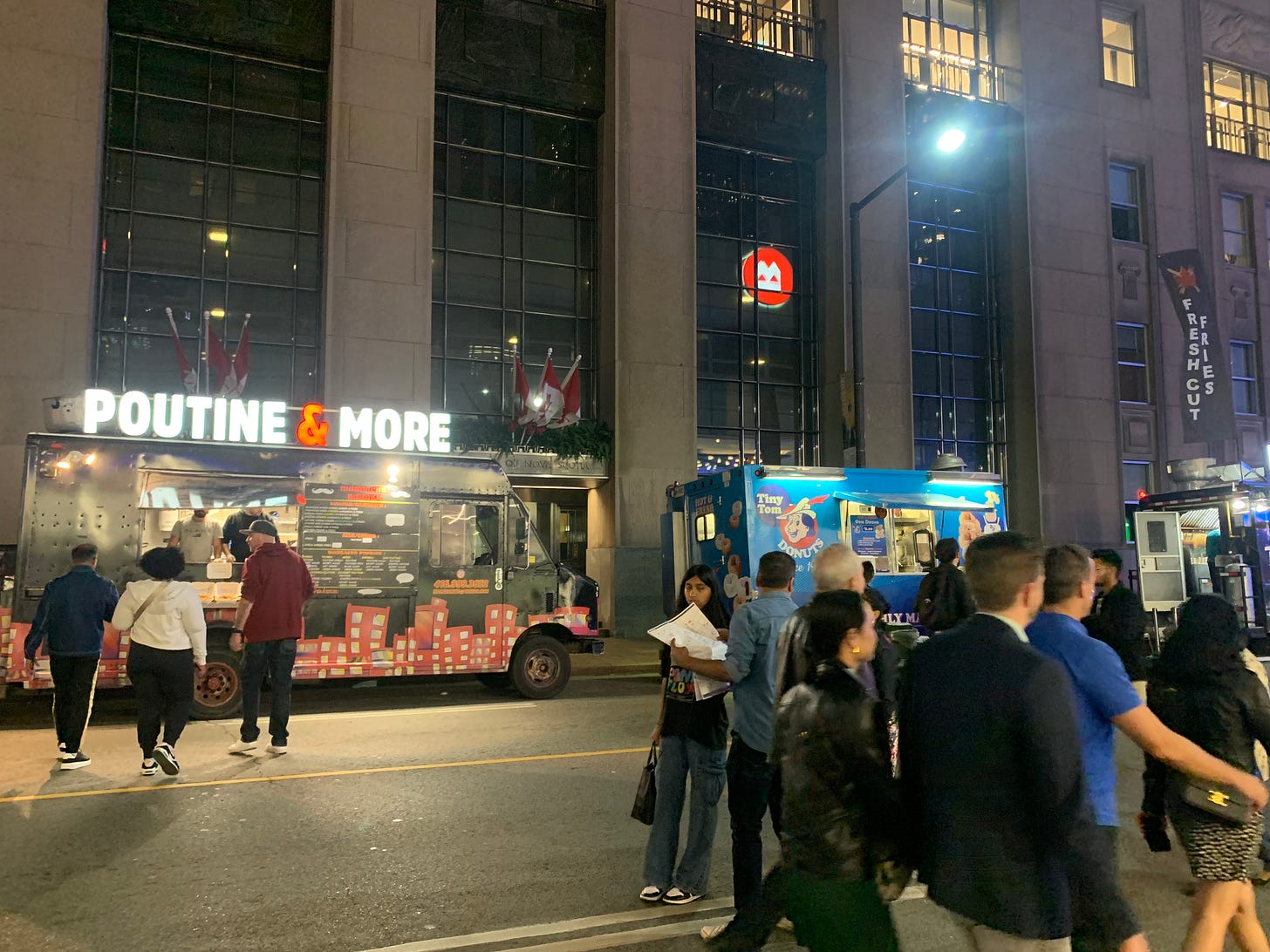 A food truck with a sign that says "Poutine & More" with red, wavy city buildings painted on a black van, and scattered crowds in front.