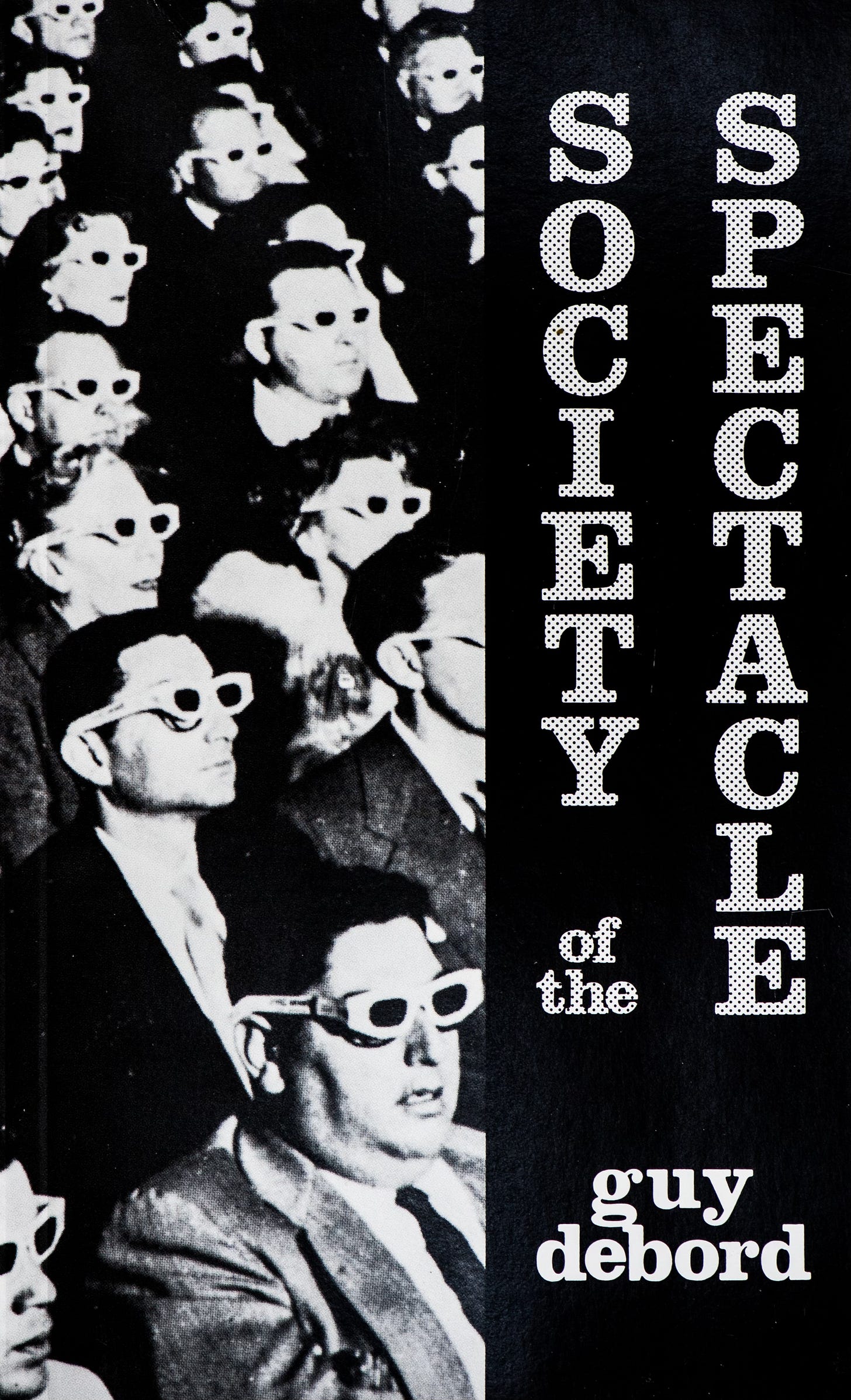 The black and white cover of Guy Debord’s Society of the Spectacle. On the left half is a famous image of a movie audience wearing stark 3-D glasses, gazing at a screen we can’t see. On the right is a band with the title in a 70s style font.