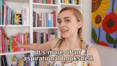 GIF of Hannah in front of her bookshelves saying "it's more of an aspirational bookshelf"