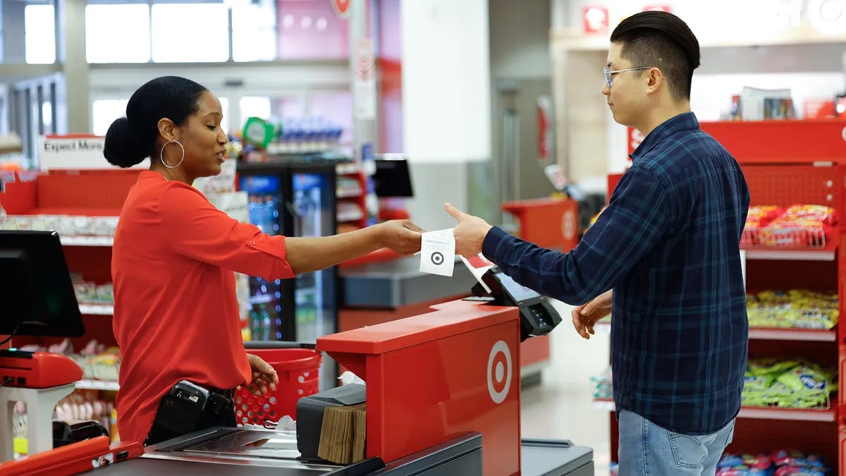 A Target employee completes an in-store checkout purchase and hands a customer a receipt.