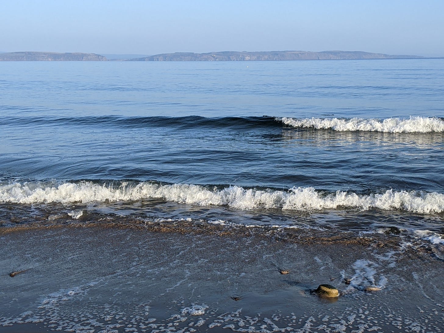 Waves gently lap at the beach with hills beyond at Nairn beach