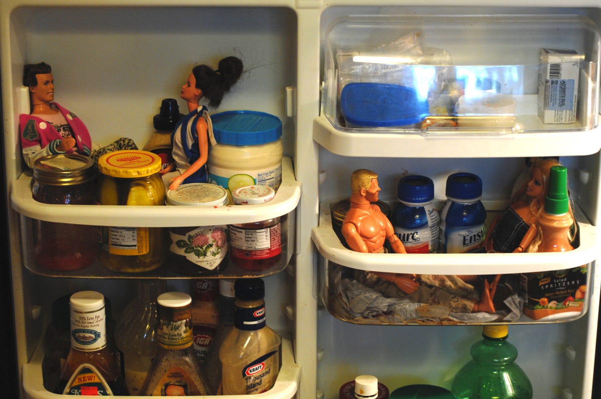 The inside of a refrigerator door, crowded with condiments, but also two scenes of Barbies and G.I.Joe dolls on "dates", apparently lost in conversation with each other.