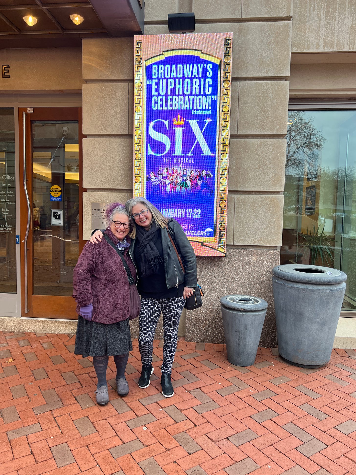 Sarah and Sara outside the Bushnell theater with Six the Musical invite in background