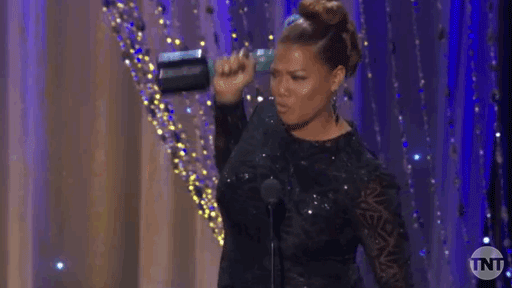GIPHY of Queen Latifah in a Black gown accepting an award & raising it above her head.
