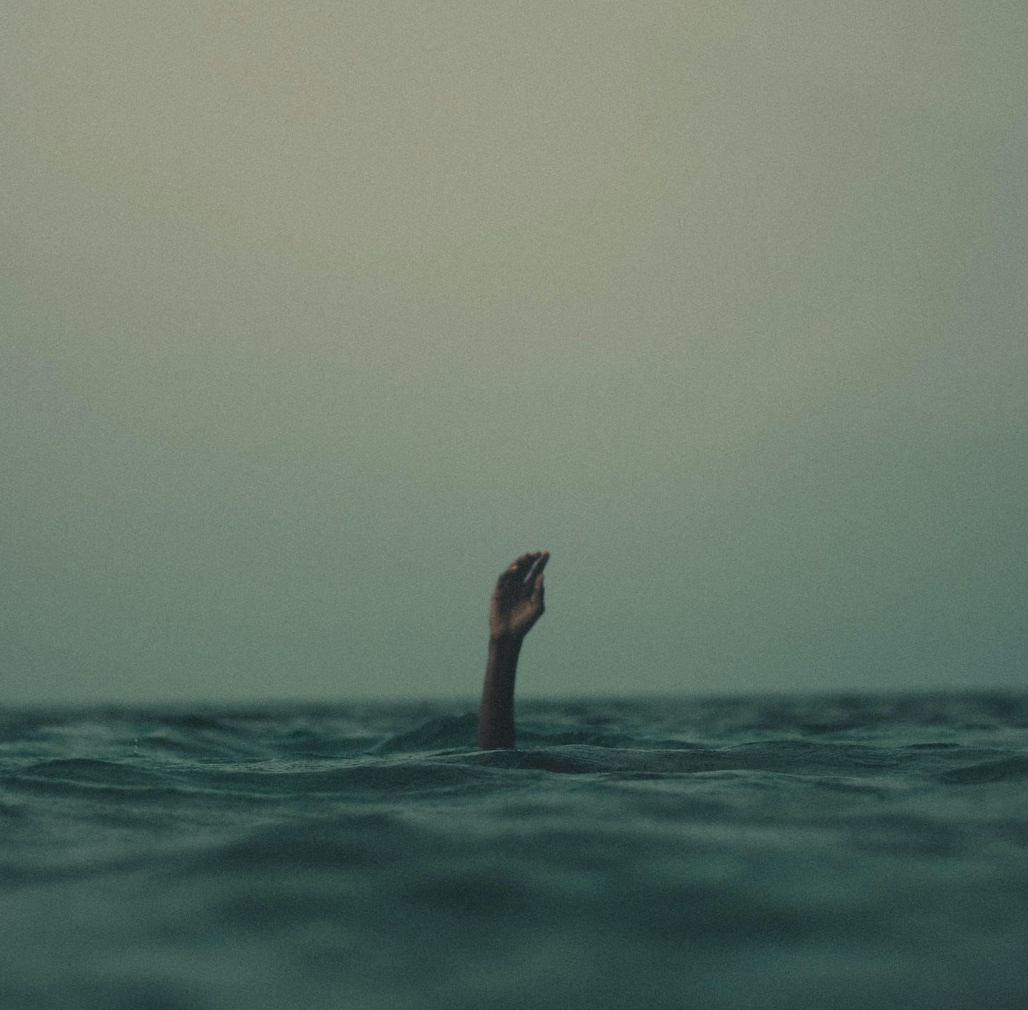 A hand reaches out of the ocean against a pale blue sky