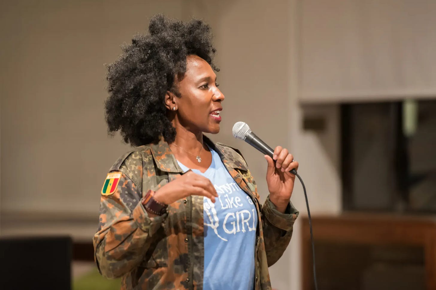 A Black woman wearing a camo jacket speaks into a mic.