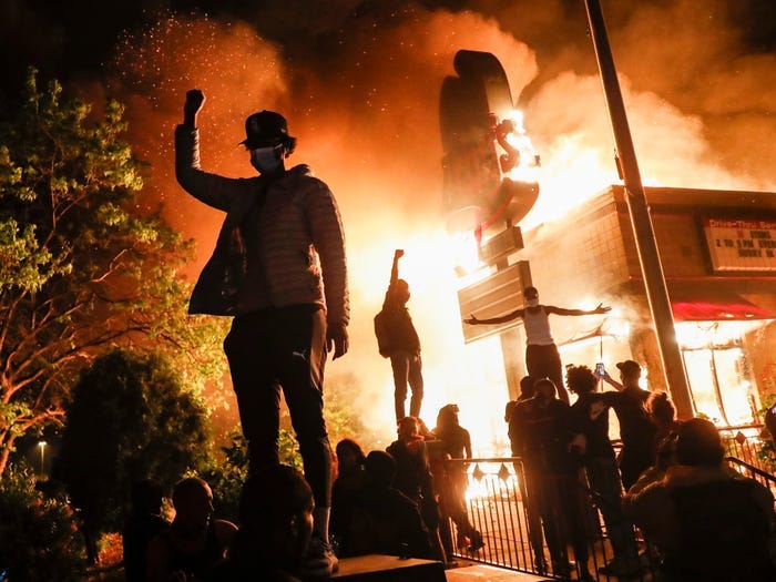 Protestors demonstrate outside of a burning fast food restaurant, Friday, May 29, 2020, in Minneapolis. Protests over the death of George Floyd, a black man who died in police custody Monday, broke out in Minneapolis for a third straight night. (AP Photo/John Minchillo)