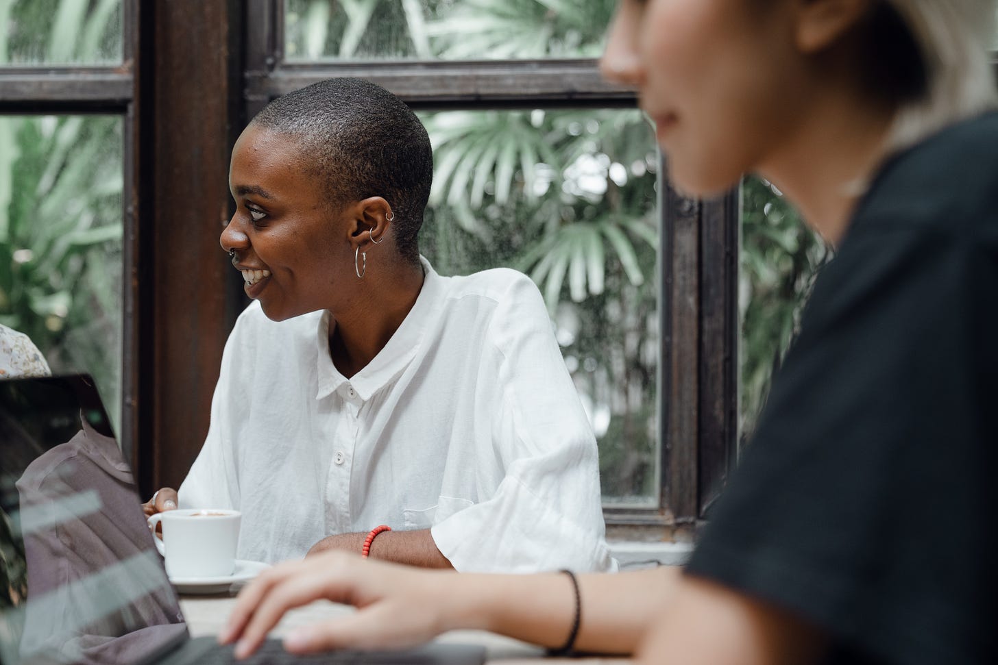 optimistic young diverse female colleagues working on laptop and drinking coffee