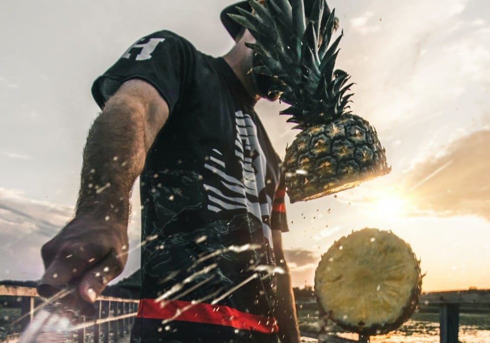 Man on a pier at sunset slashing a pineapple in half midair