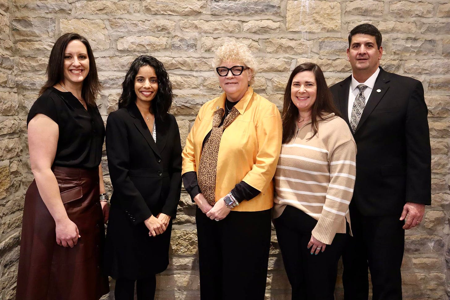 The five members of the Board of Education posing for a photo against a light colored brick wall