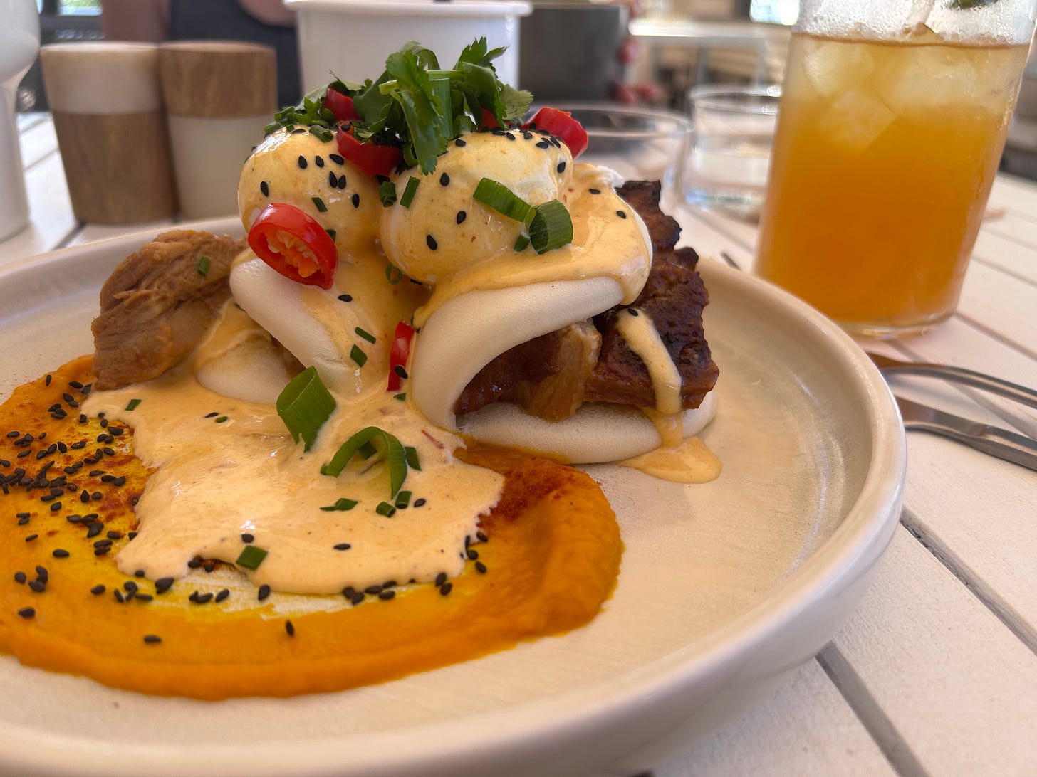 A plate of laksa eggs Benedict, with bao and pork, plus a glass of iced tea.