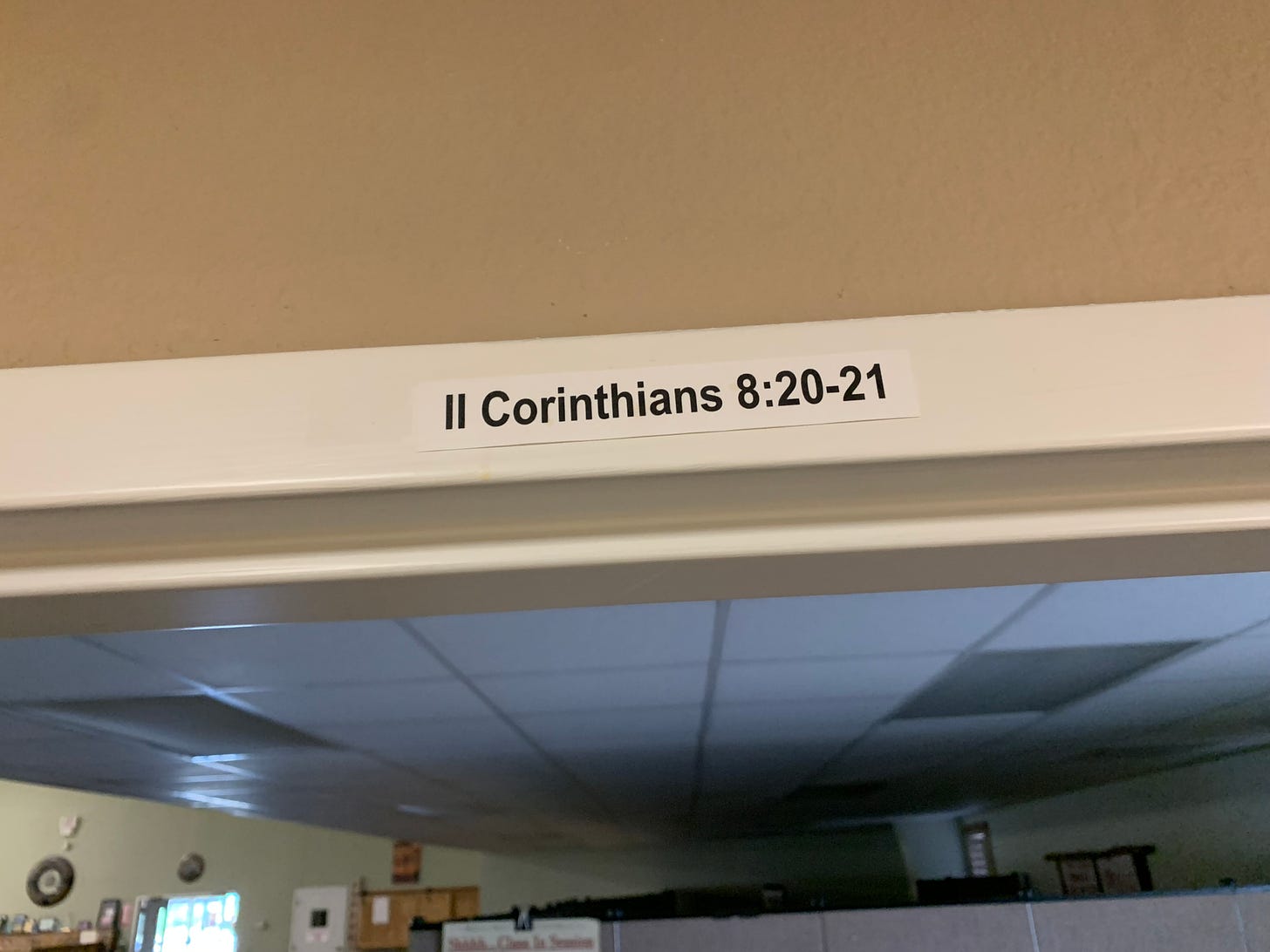 Image of a Bible reference from 2 Corinthians 8:20-21 taped above an office door.