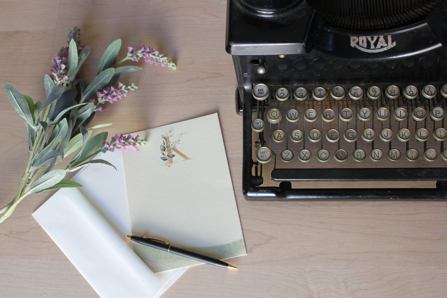 Fresh flowers and stationery on a wooden desk next to a vintage typewriter.