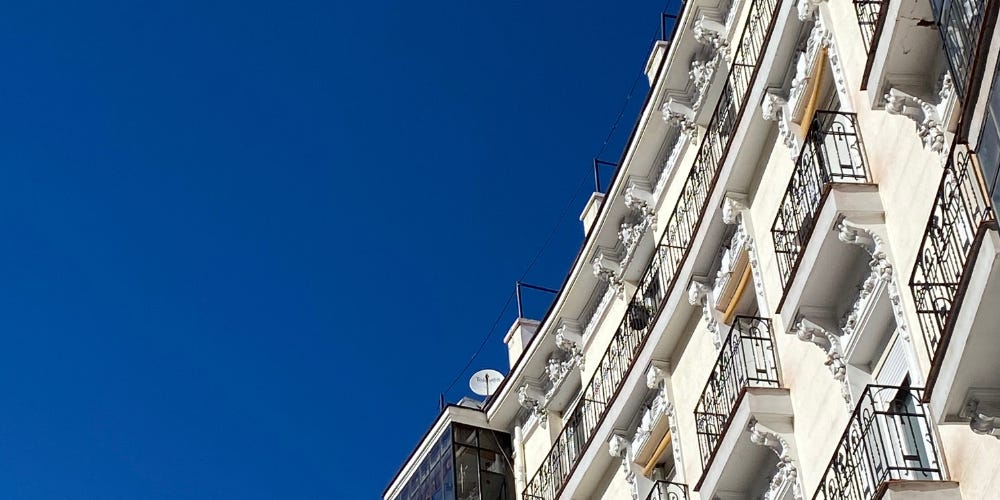 An angled photo of a white apartment building with ornate iron balconies against a blue sky