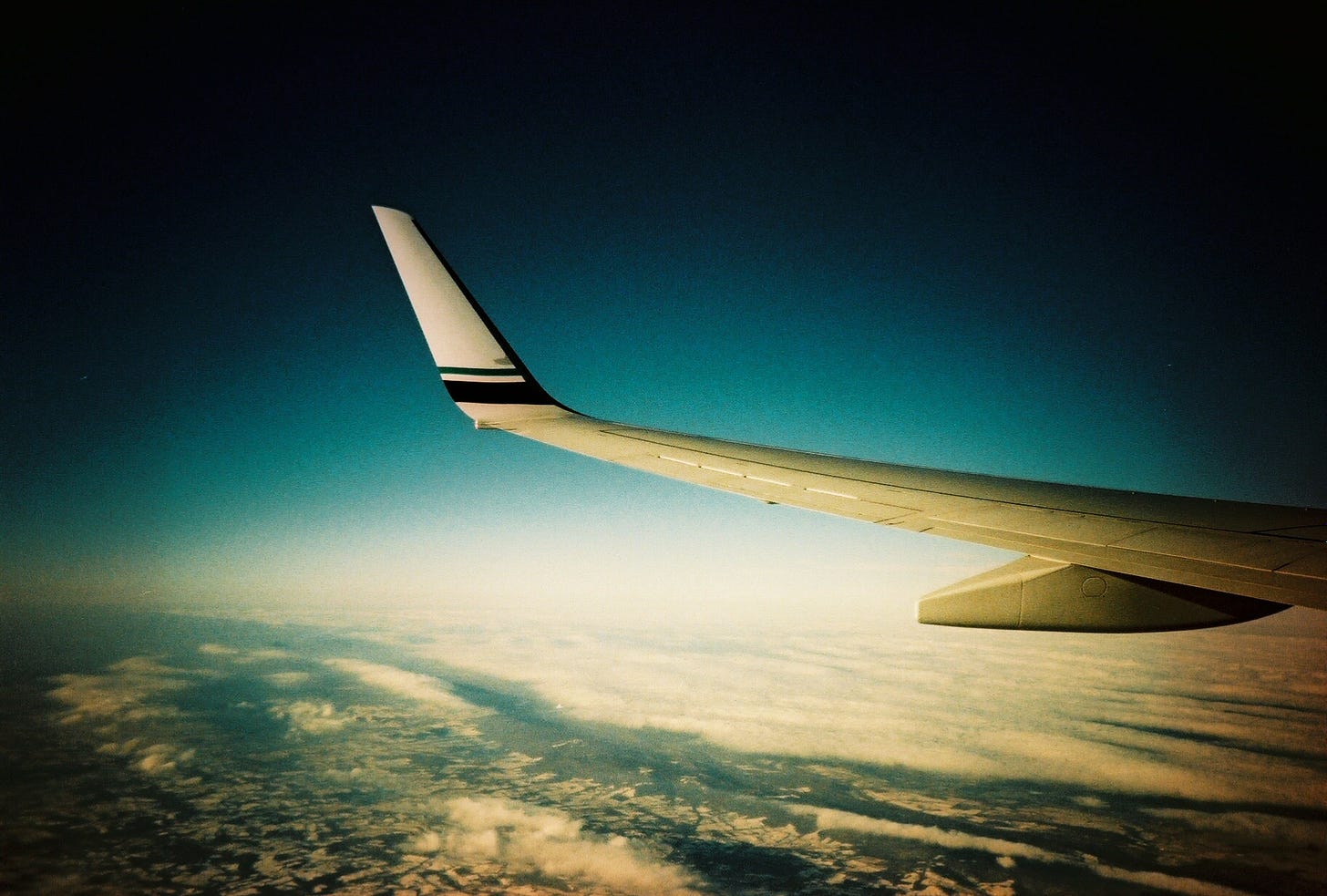 A photograph taken while looking out an airplane window, at the airplane's wing, with the ground far below.