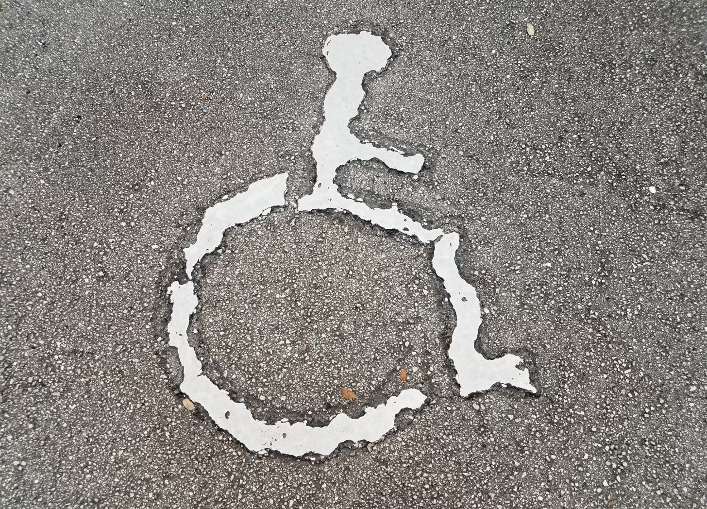 Rough, eroded wheelchair symbol painted on pavement