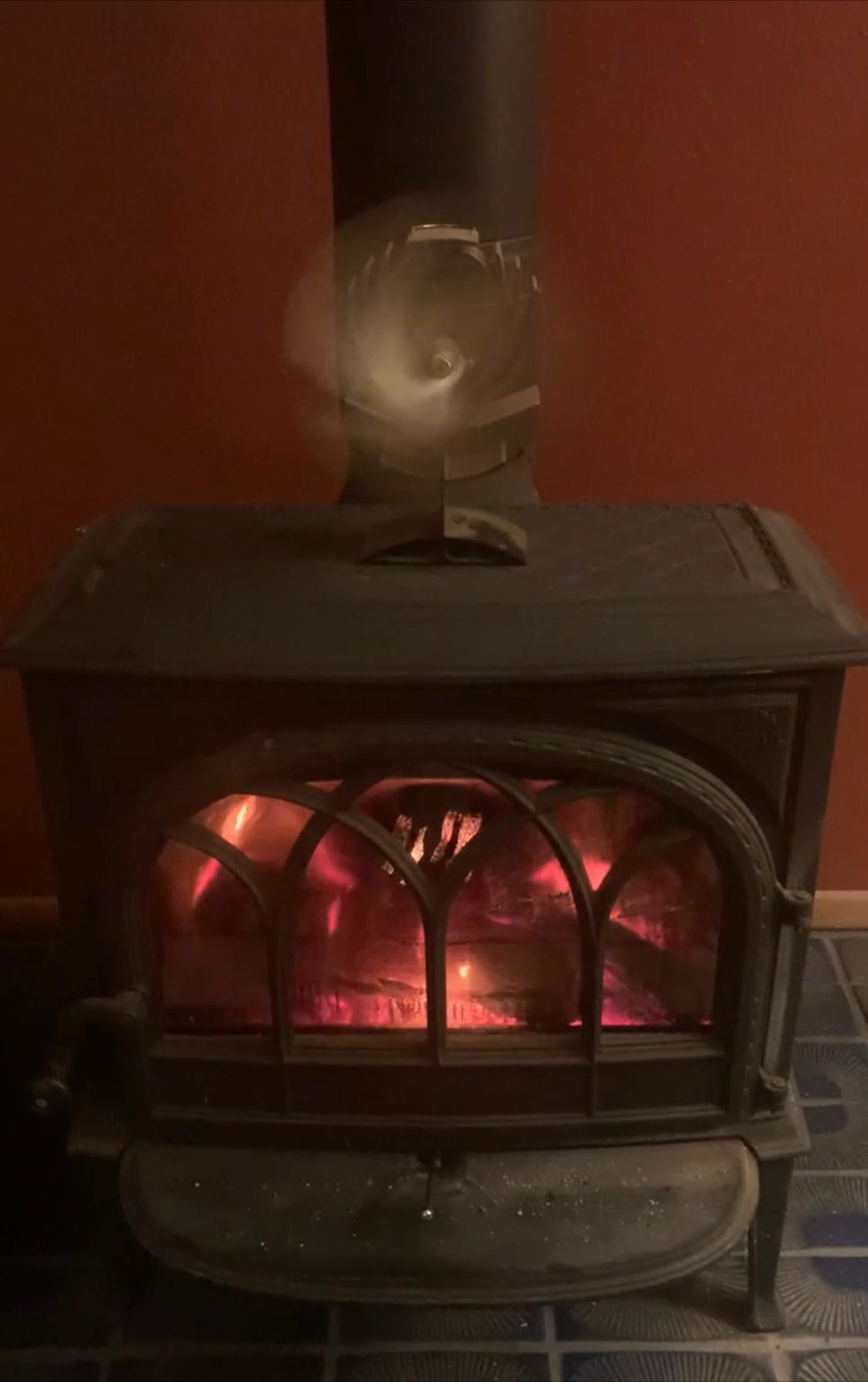 A fire in a cast iron stove with a heat-operated fan spinning atop it.