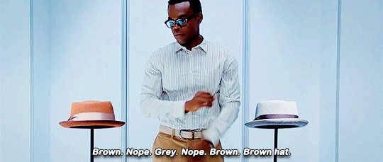 Chidi from The Good Place struggling to decide between a brown and a grey hat.