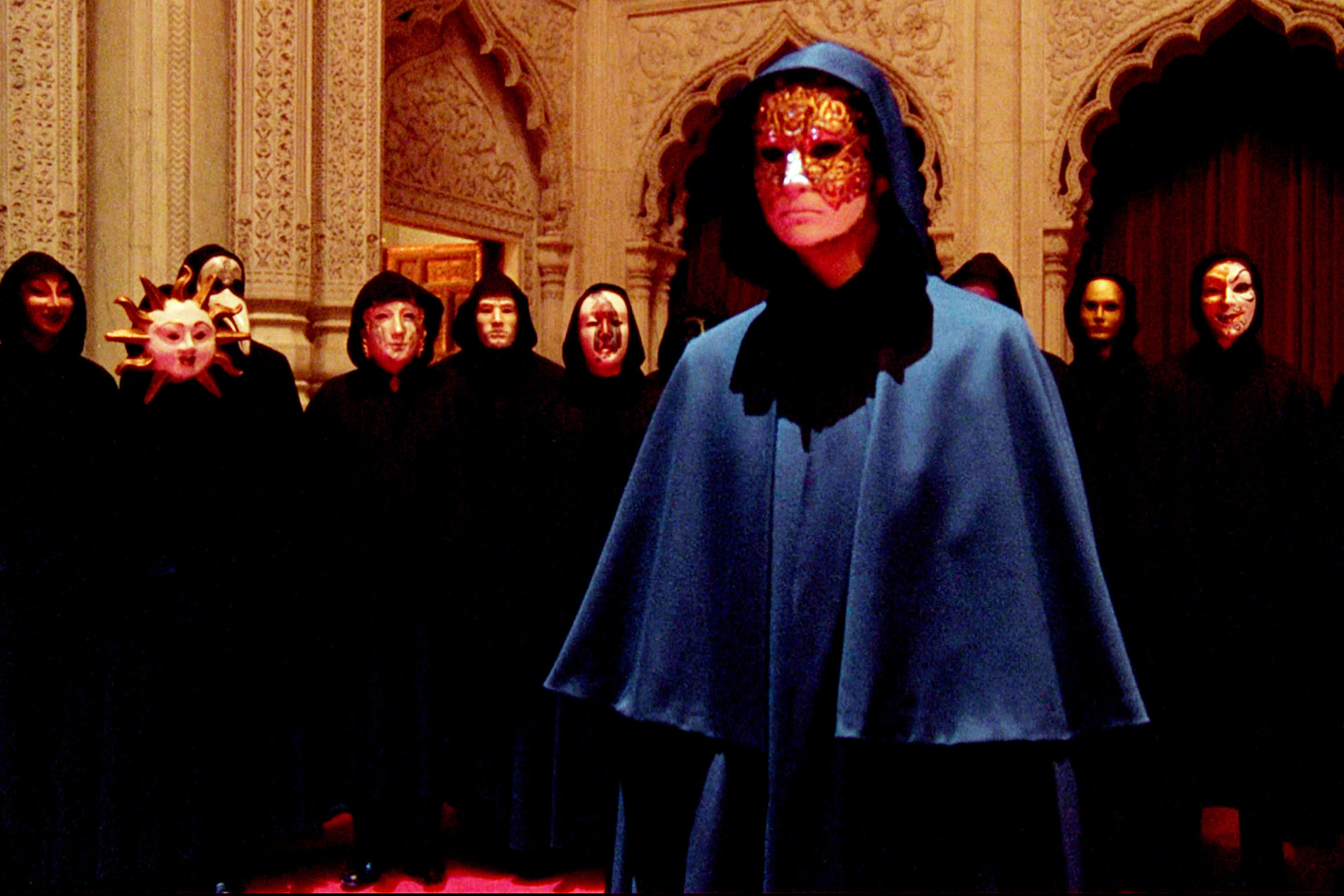 Still from Eyes Wide Shut, people in capes and weird illuminati masks in a baroque-looking room