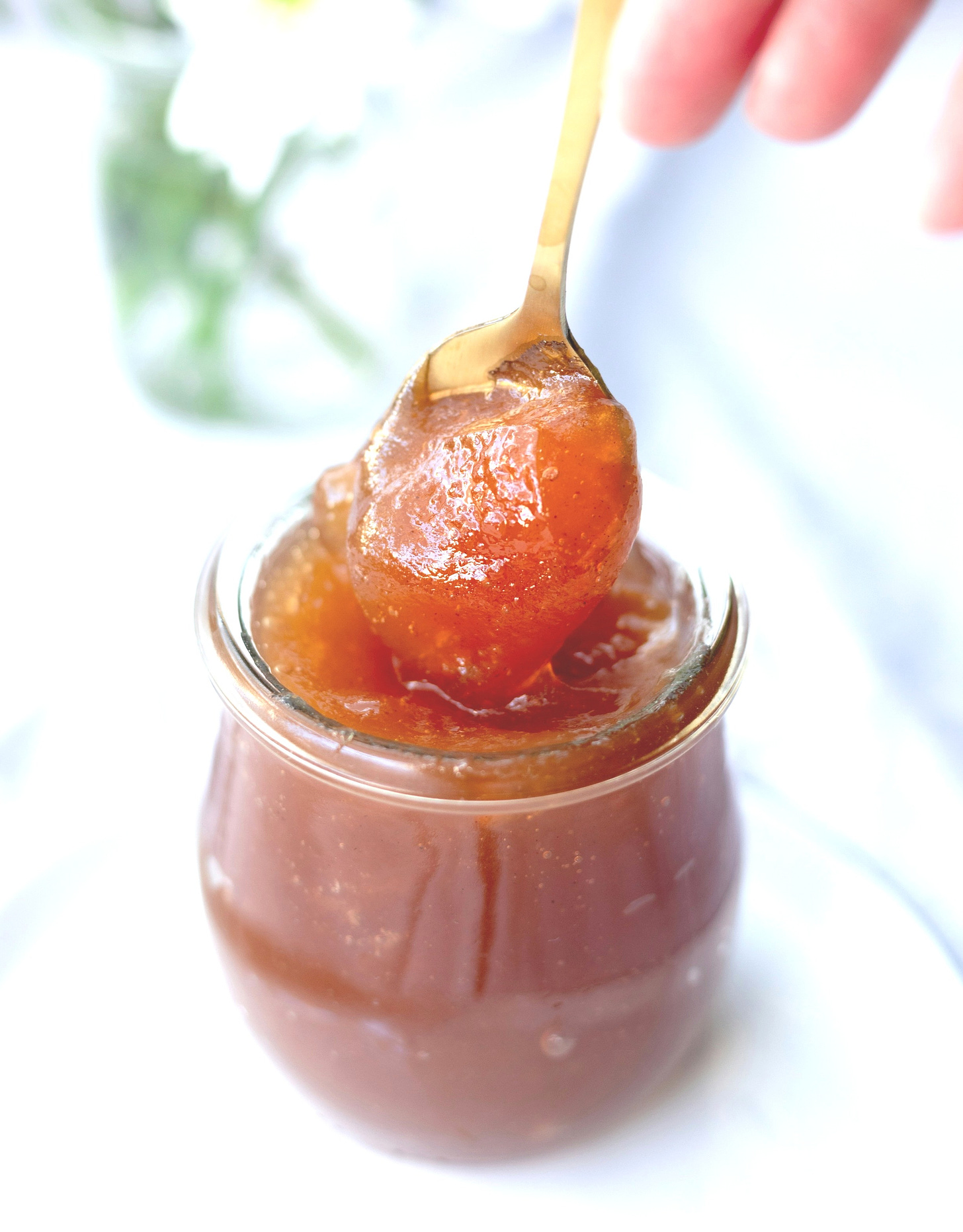 weck-style jar with orange coloured jam, a golden spoon scoops out some of the jam, clear vase in background