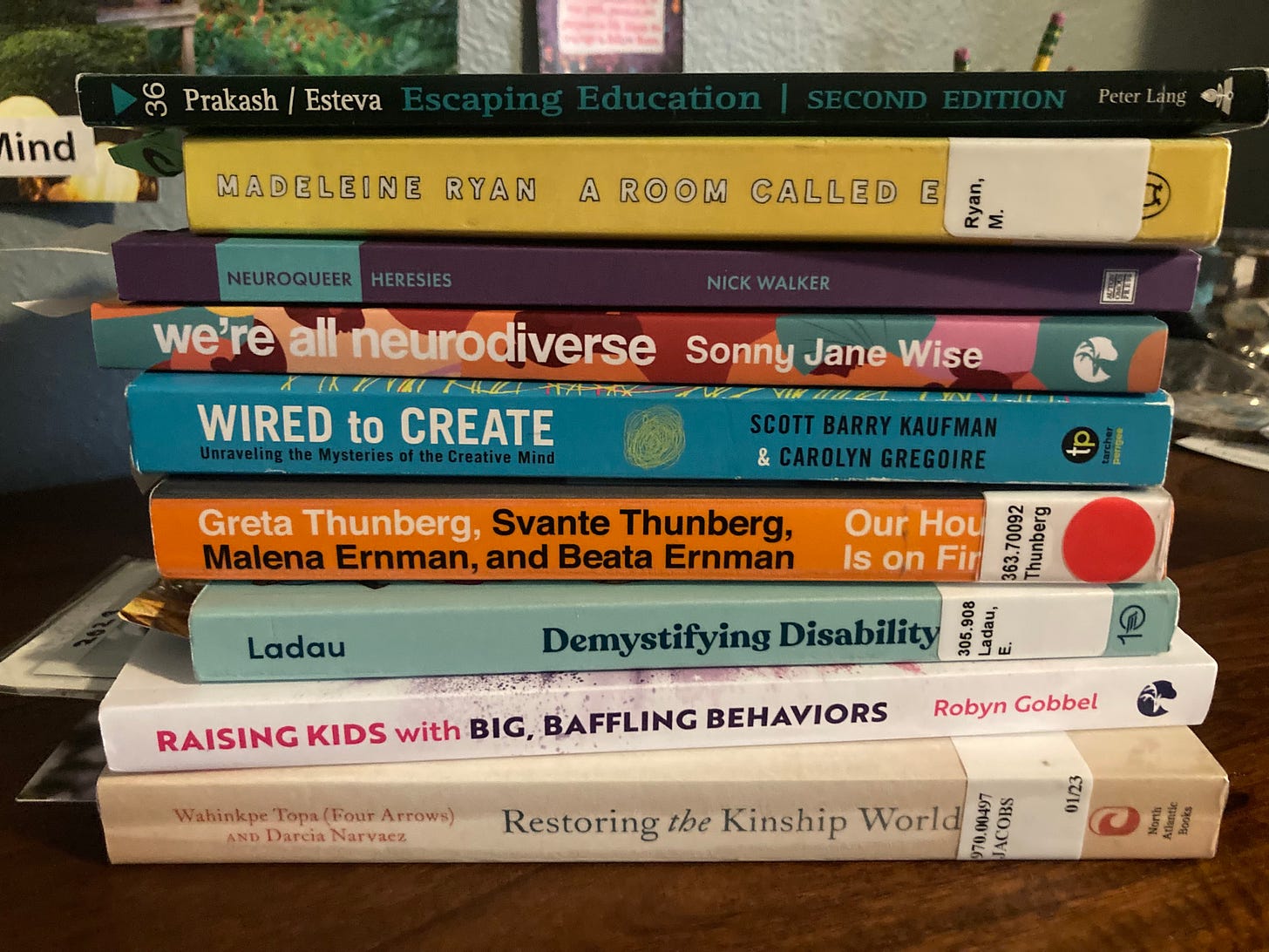 Image is a stack of nine books titled: Escaping Education, A Room Called Earth, Neuroqueer Heresies, We're All Neurodiverse, Wired to Create, Our House is On Fire, Demystifying Disability, Raising Kids with Big, Baffling Behaviors, and Restoring the Kinship Worldview