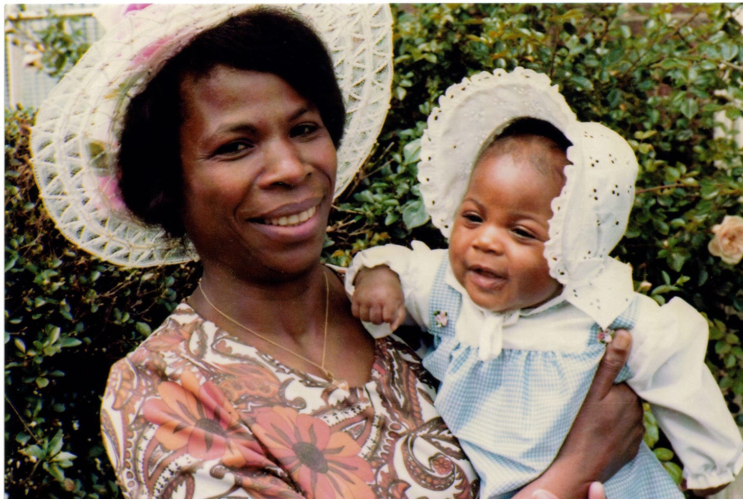 Black woman wearing a hat and holding a black baby girl wearing a bonnet