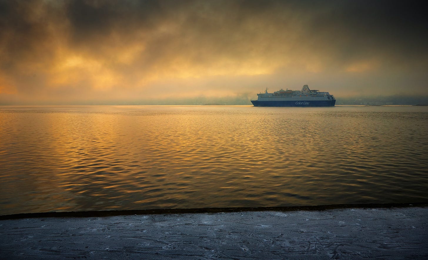 A blue and white ocean liner sailing the open waters in the background. The sky is a golden color and is reflected in the water.
