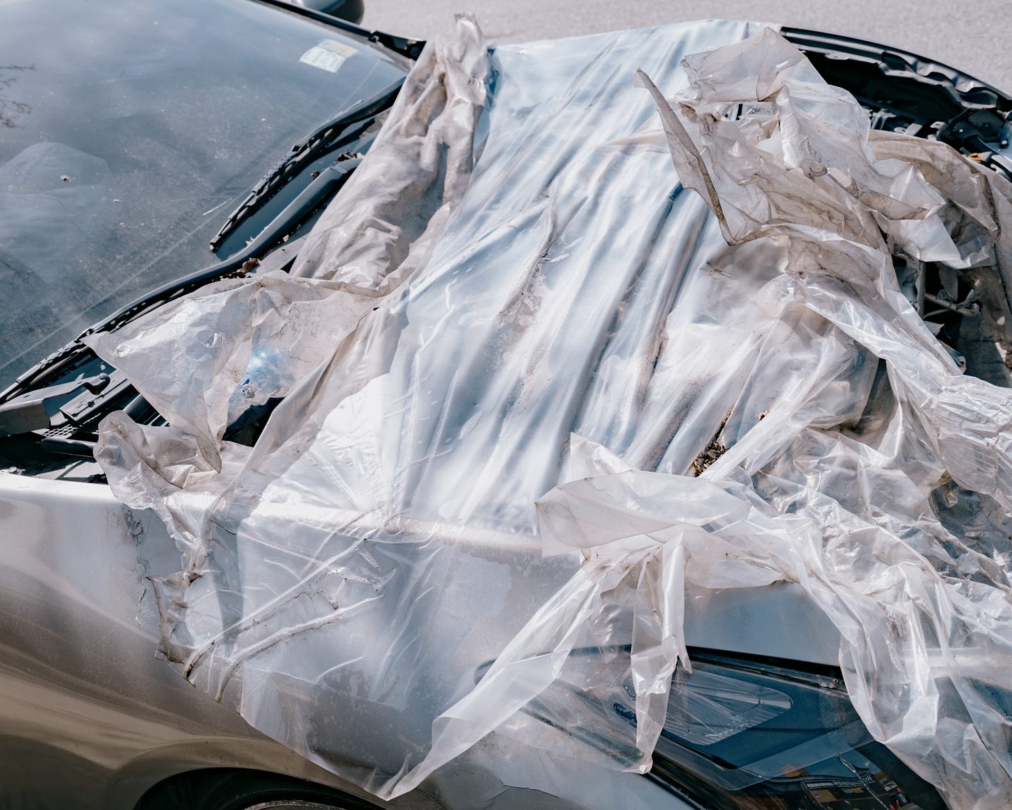 Plastic tarp covers exposed engine of wrecked car