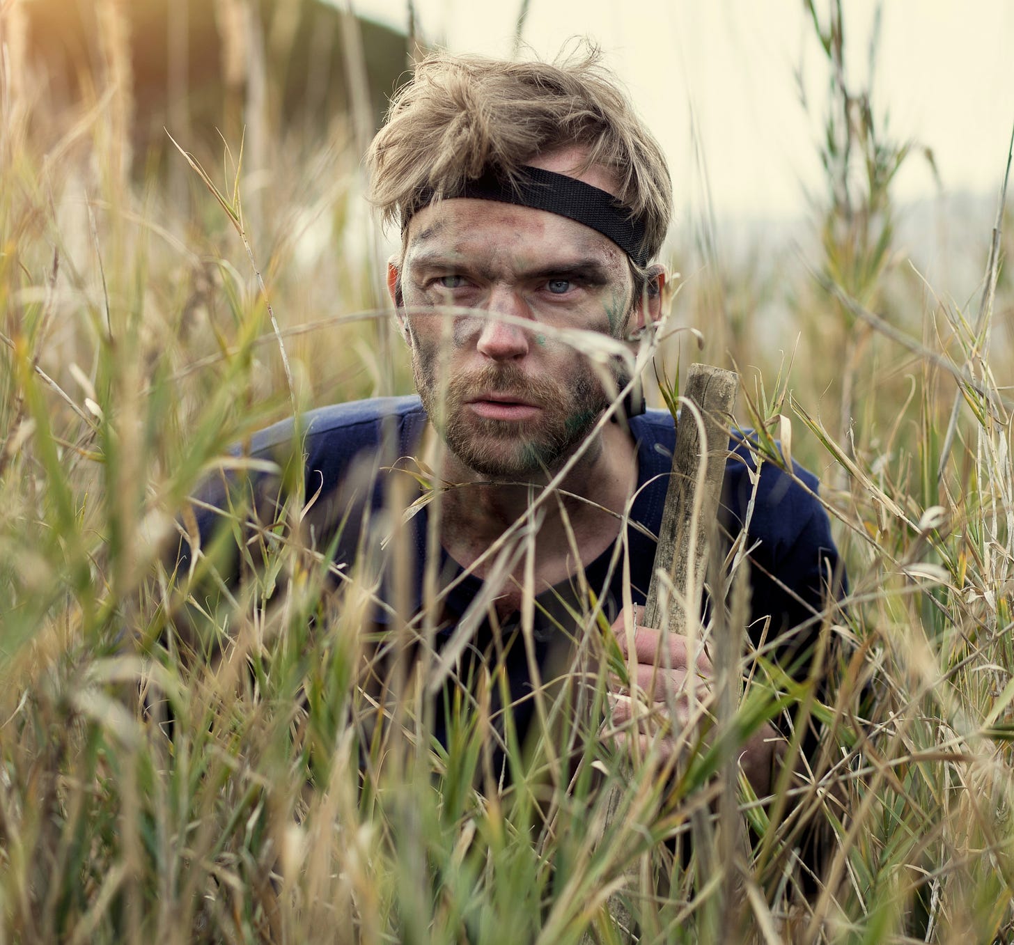 Tense, dirty soldier hiding in the grass