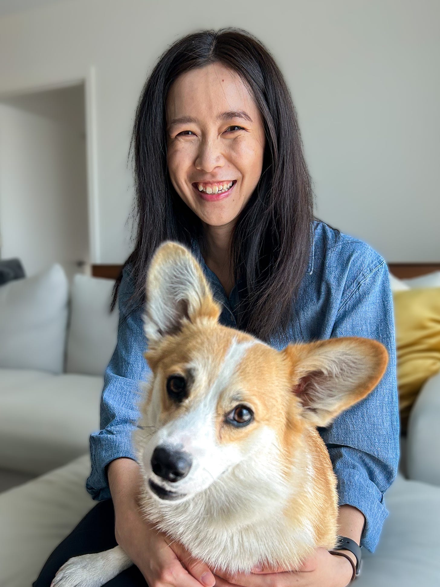 Woman with black hair smiling at the camera with a corgi on her lap