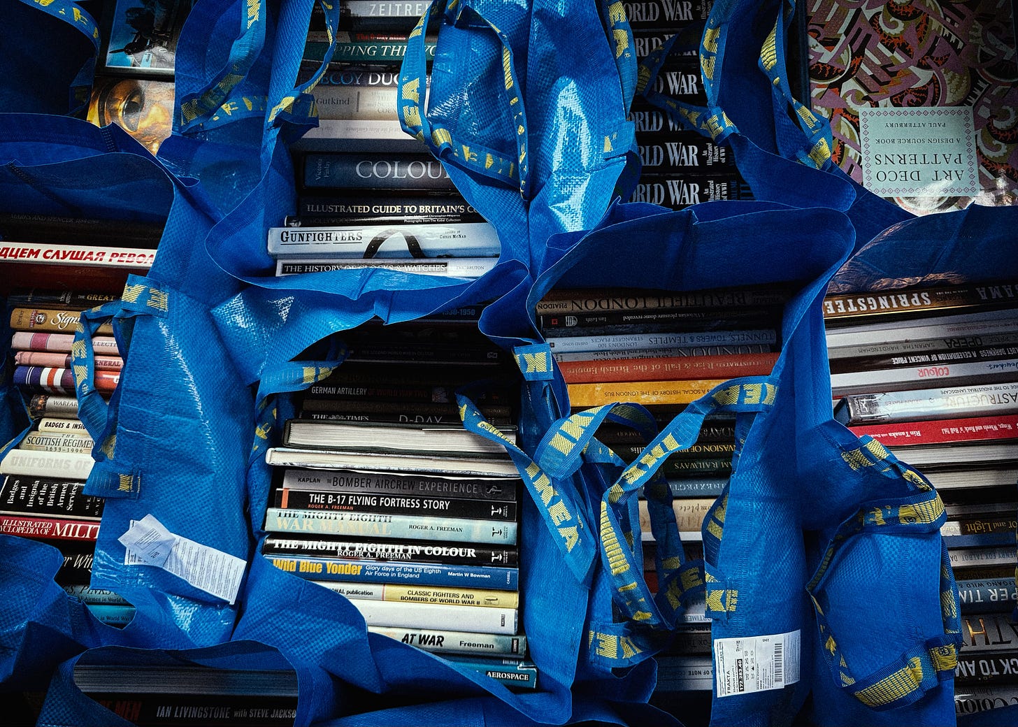 Photograph shows stacks of oversized books contained in blue IKEA bags.