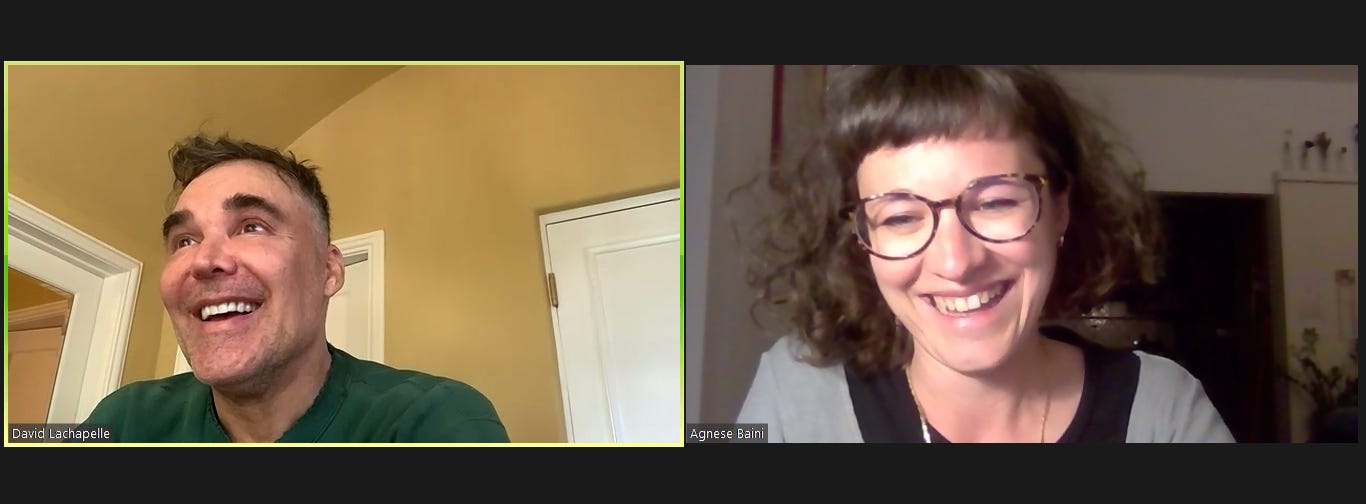 Screenshot di una chiamata zoom tra due persone, entrambe stanno ridendo. La persona a sinistra, David LaChapelle, è in una stanza dalle pareti gialle e indossa una maglia verse. La persona a destra sono io, Agnese Baini, con una maglia nera e azzurra e sono dentro una stanza buia e si intravedono delle piante