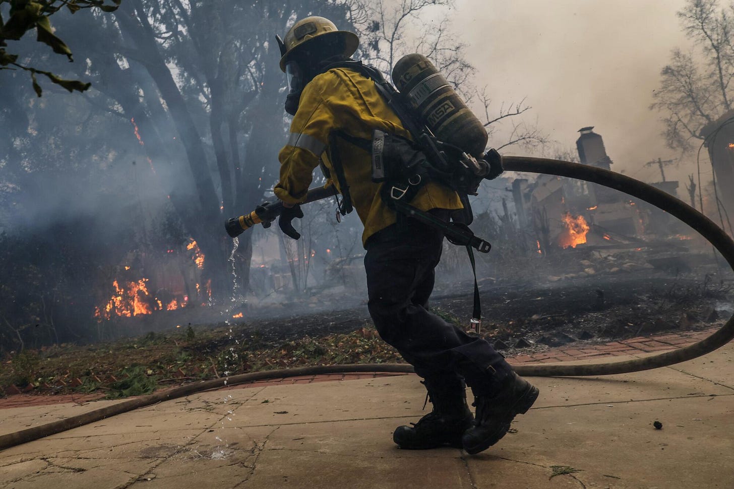 A firefighter carries a hose while battling a fire. 
