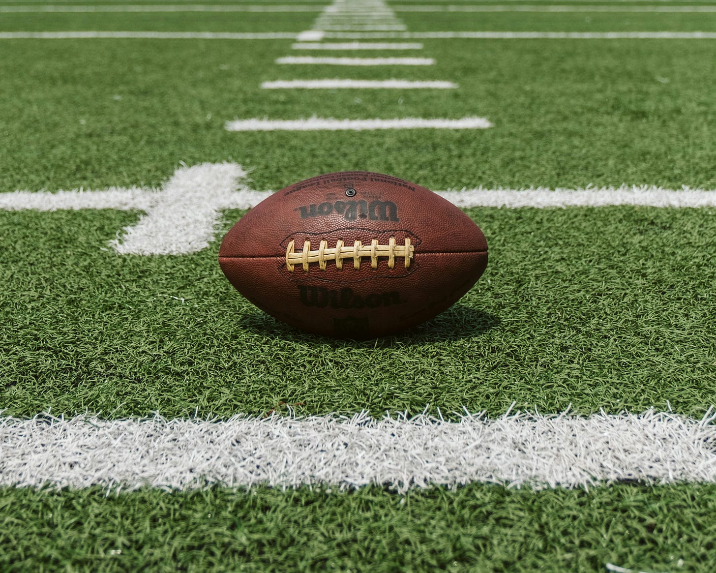 A brown football lying on a green and white football field.