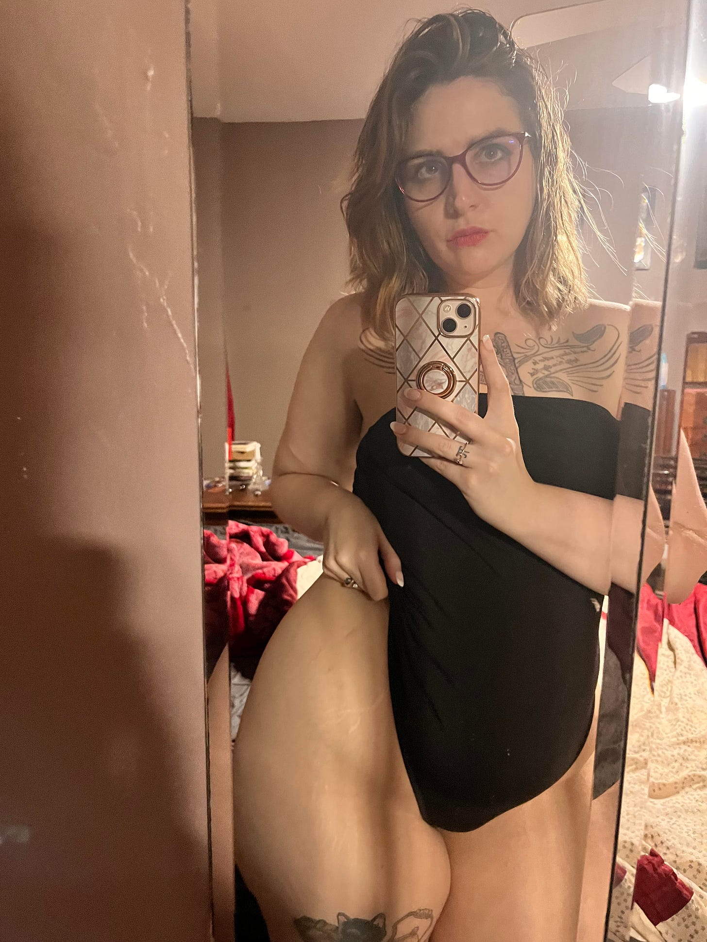 author being an unabashed thirst trapping whore with a clearly dirty room, wearing one-piece black suit with phone and glasses and showing off thicc thighs
