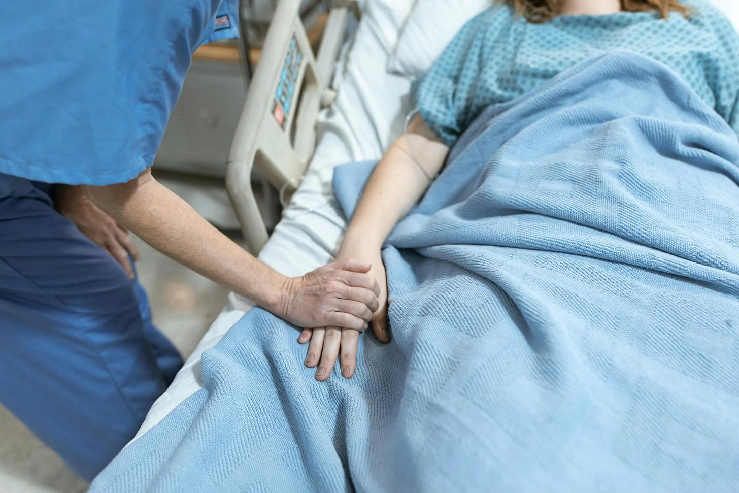 Nurse holds a patients hand in a hospital bed.