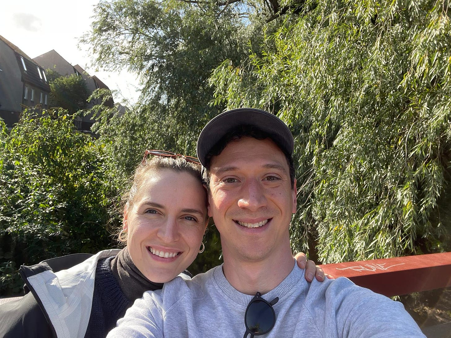 Two people standing on a bridge with greenery in the background on a sunny day