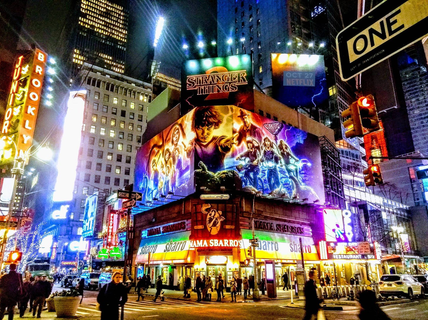 Times Square at night from street level, looking up at a very large billboard advertising Stranger Things, the Netflix series