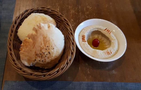 a basket of pita bread with a dish of homemade hummus beside it