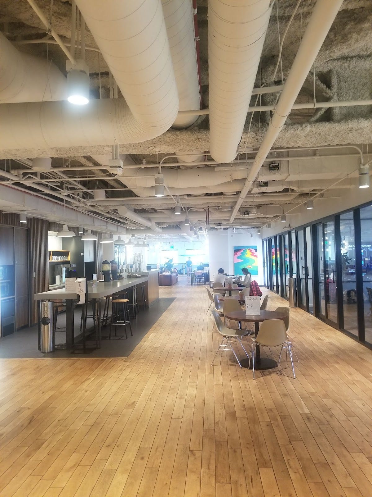 mostly empty wework office with kitchen, tables, and phone booths