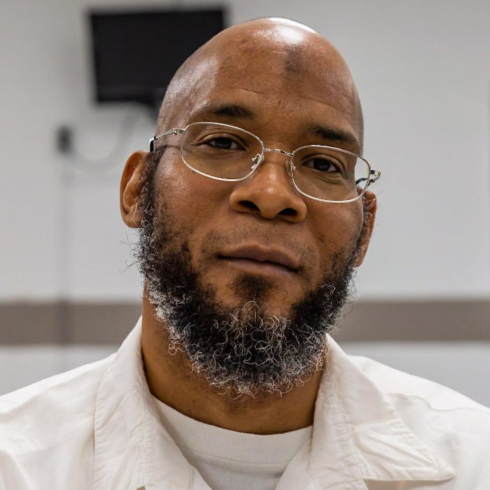 Photo of Marcellus Williams- a Black man with glasses, a bald head, salt and pepper beard. Wearing a white button up shirt