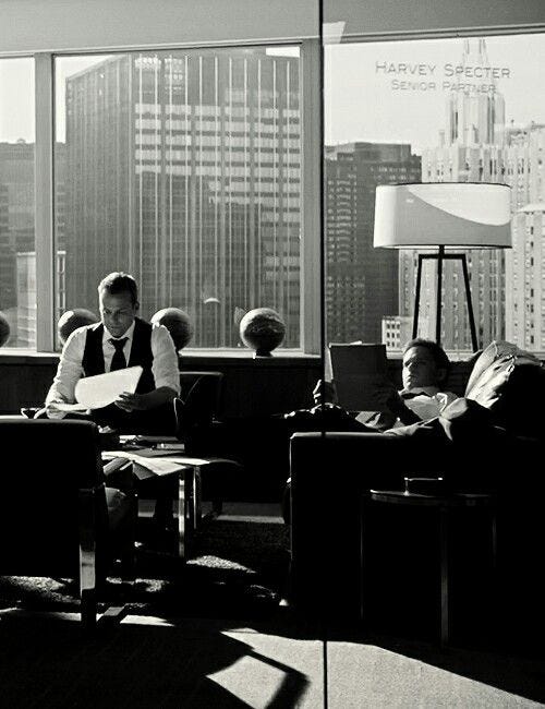 This may contain: black and white photograph of people sitting at desks in an office with large windows