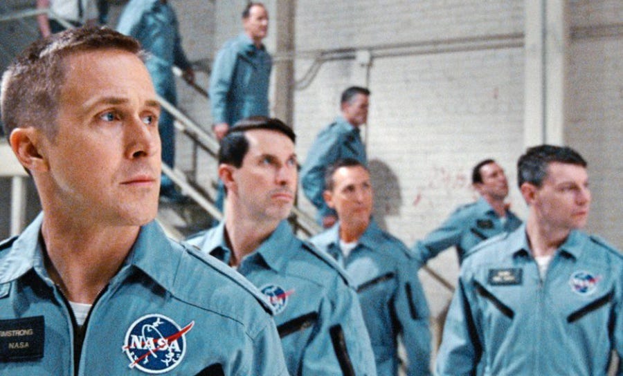 Ryan Gosling as Neil Armstrong in First Man. Standing with other astronauts looking at something off camera.