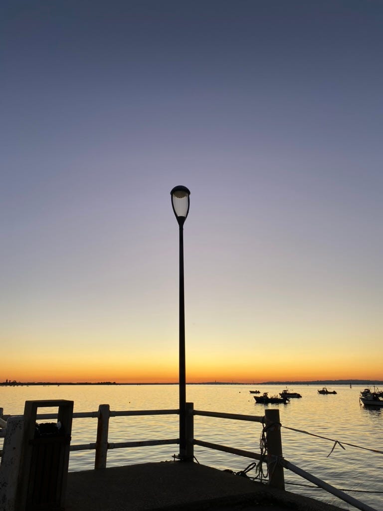 A lamposts on a pier with boats on a river at sunset