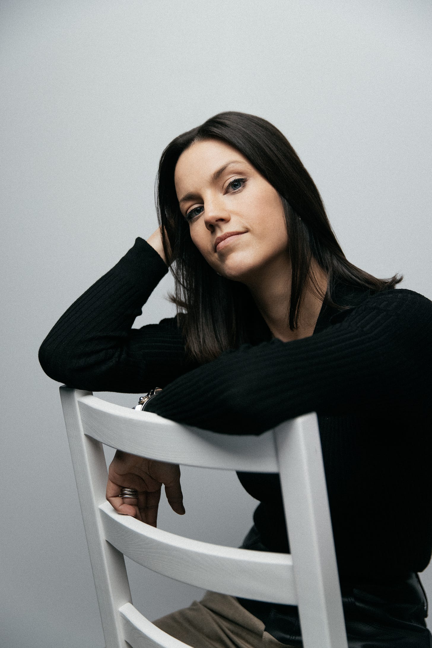Portrait of marketer Julianne Fraser. She is wearing a black long-sleeved top and is sitting in front of a white background on a white chair.