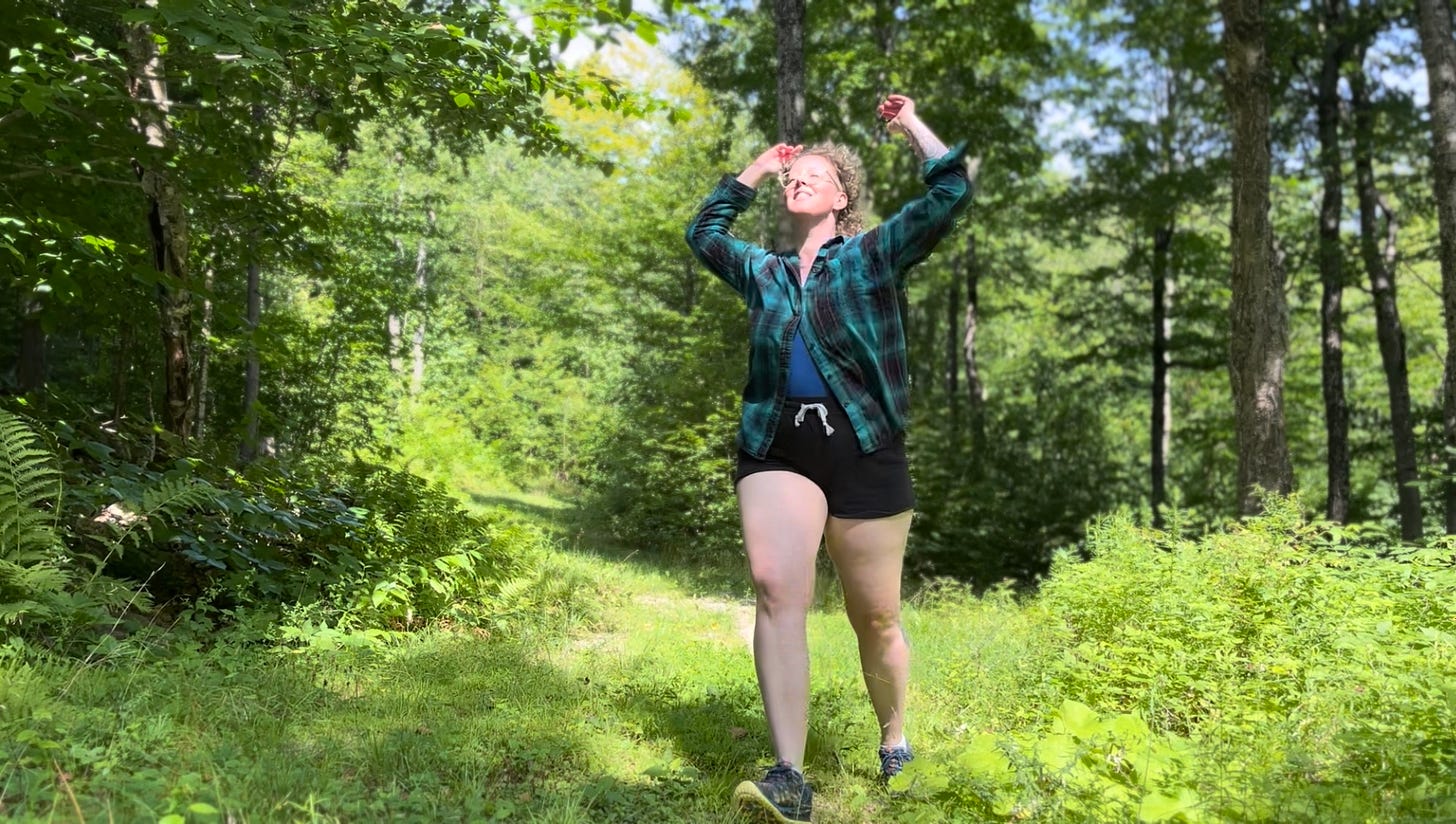 a person in motion facing the bright sun in a lush green wood, legs locomoting, arms thrown upward, face opening