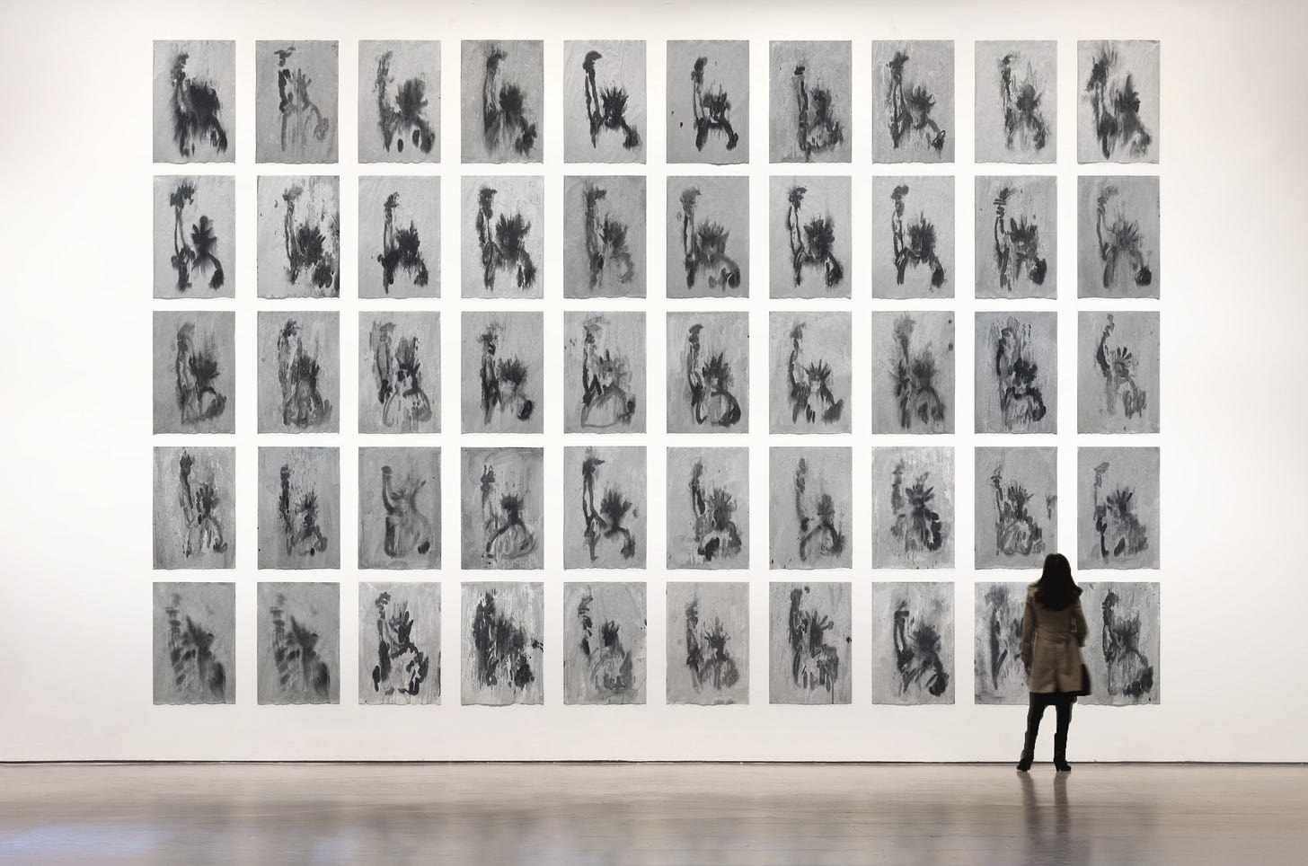 A person stands in front of a wall with 50 varied images in black and gray of the Statue of Liberty