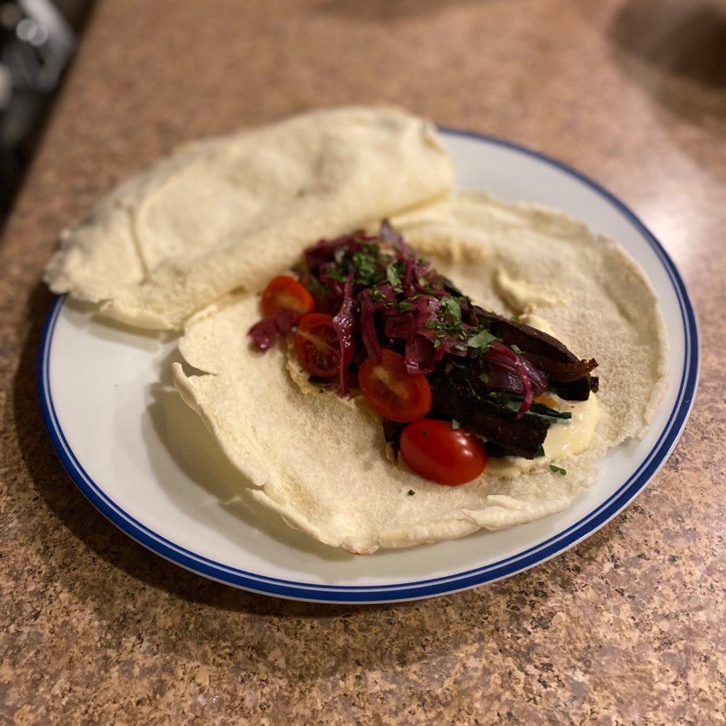a pita torn open and filled with the shawarma described above, hummus, yogurt, kale, pickled red cabbage, and halved grape tomatoes.